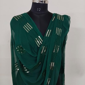 May include: A dark green scarf with gold sequin and stripe detailing. The scarf is draped over a black mannequin. The mannequin has a silver neck and the number 12 is printed on the neck.