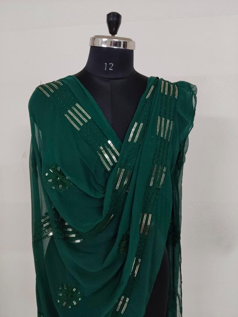 May include: A dark green scarf with gold sequin and stripe detailing. The scarf is draped over a black mannequin. The mannequin has a silver neck and the number 12 is printed on the neck.