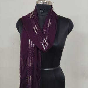 May include: A dark purple scarf with silver embellishments is draped over a black mannequin. The scarf has a rectangular shape with decorative silver lines and patterns along the edges. The mannequin has a silver neck piece with the number 12.