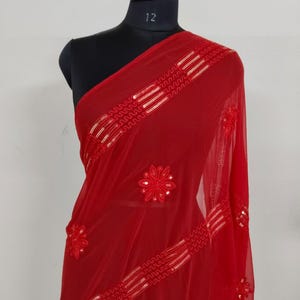 May include: A vibrant red sheer scarf draped over a mannequin. The scarf features intricate floral embroidery and horizontal bands of gold sequins. The fabric is lightweight and flowing, with a delicate texture. The scarf is a beautiful accessory.