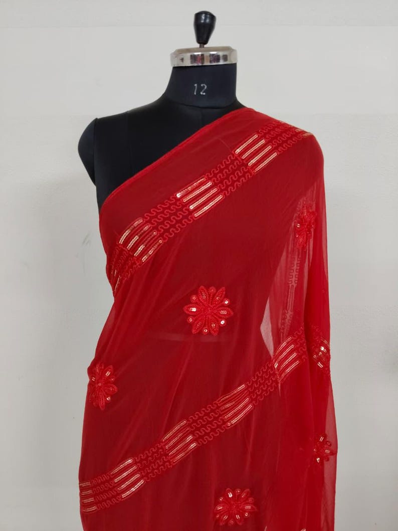 May include: A vibrant red sheer scarf draped over a mannequin. The scarf features intricate floral embroidery and horizontal bands of gold sequins. The fabric is lightweight and flowing, with a delicate texture. The scarf is a beautiful accessory.