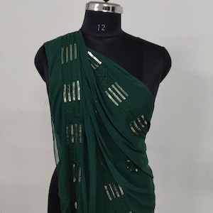 May include: A dark green, one-shoulder garment draped over a black mannequin. The fabric is embellished with vertical rows of silver sequins. The garment is likely a shawl or a piece of formal wear.
