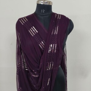May include: A draped, plum-colored scarf with silver sequin embellishments. The scarf is displayed on a black mannequin, showcasing its flowing fabric and decorative details. The sequins are arranged in vertical and horizontal patterns.