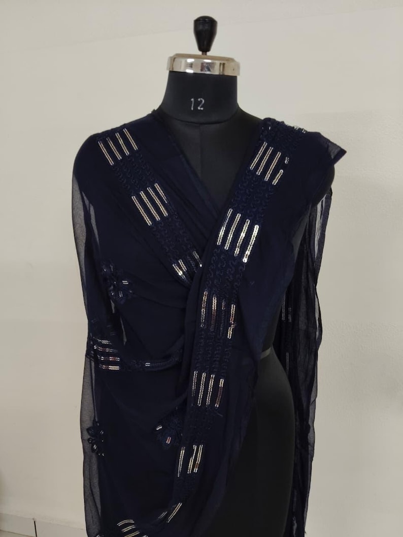 May include: A navy blue sheer scarf with silver sequin embellishments. The scarf is draped over a mannequin, showcasing the rectangular sequin patterns. The fabric appears lightweight and flowing, suitable for formal wear or adding a touch of elegance.