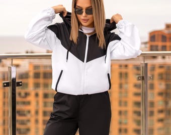 May include: A black and white hooded jacket with a chevron design, paired with black pants and black boots. The jacket has a white body and black accents. The pants are loose-fitting. The boots are lace-up.