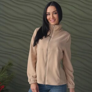 May include: A beige fleece jacket featuring a high collar, a full-length front zipper, and long sleeves with elasticized cuffs. The jacket is paired with blue denim jeans, creating a simple and functional outfit for cooler weather conditions.