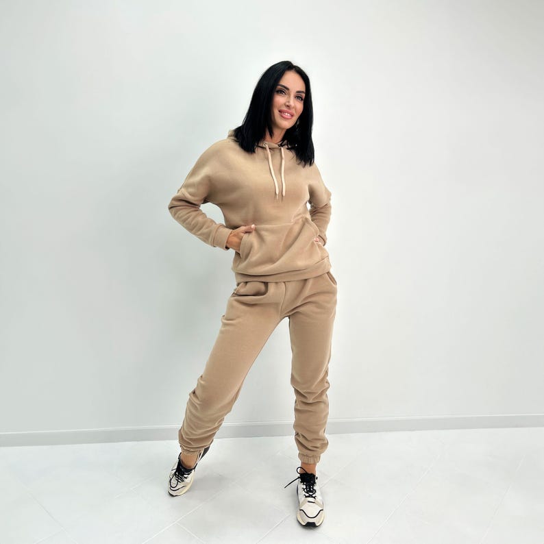May include: A tan-colored hoodie and sweatpants set. The hoodie has a drawstring and a front pocket. The sweatpants have pockets and a relaxed fit. The outfit is made of a soft, comfortable material, perfect for casual wear.