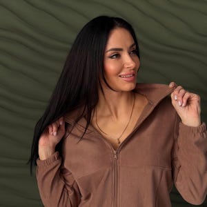 May include: A solid brown fleece jacket featuring a high collar, a full-length front zipper closure, and long sleeves with elasticized cuffs. The garment is constructed from a soft, textured fleece material with a consistent matte finish.