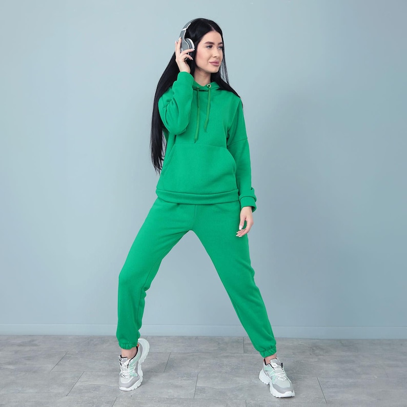 May include: A green hoodie and matching sweatpants set. The hoodie has a front pocket and a drawstring hood. The sweatpants have an elastic waistband and cuffs. The outfit is made of a soft, comfortable material.