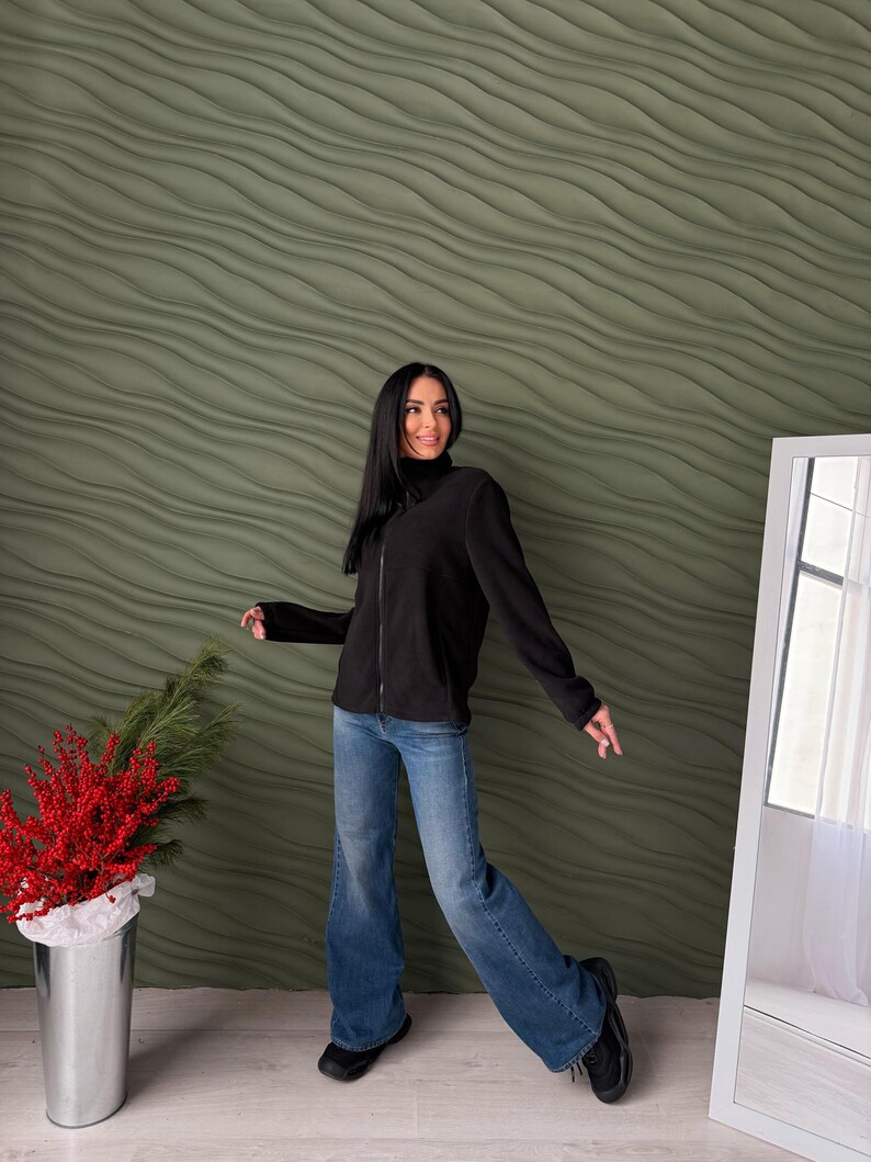 May include: A black long-sleeved fleece jacket with a full-length front zipper and a high collar, paired with blue denim jeans. The jacket features a soft texture and a simple design, while the jeans have a relaxed fit and a classic blue wash.