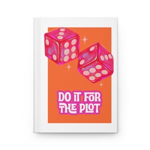 May include: A white journal with an orange background featuring two pink dice and the text "DO IT FOR THE PLOT" in pink and white. The dice have white dots.