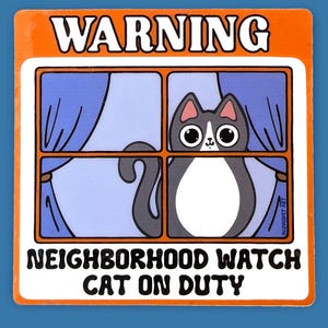 May include: Orange and white warning sign with the text "WARNING NEIGHBORHOOD WATCH CAT ON DUTY". A black and white cat with big eyes is looking out of a window with blue curtains.
