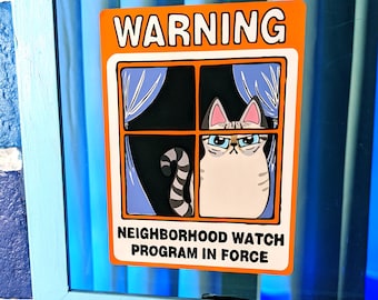 May include: A rectangular orange and white warning sign featuring a cartoon cat looking out of a window with blue curtains. The text reads WARNING at the top and NEIGHBORHOOD WATCH PROGRAM IN FORCE at the bottom in bold black capital letters.