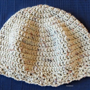 May include: A beige crocheted beanie hat with a textured pattern. The hat is made with a yarn that has a speckled appearance.