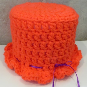 May include: Orange crocheted toilet paper roll cover with a purple ribbon tied around the bottom.