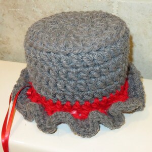 May include: Gray crocheted toilet paper roll cover with a red crocheted ruffle around the bottom. A red ribbon is attached to the side.