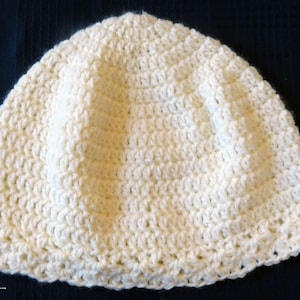 May include: A white crocheted beanie hat. The hat is made with a simple stitch pattern and has a rounded crown.