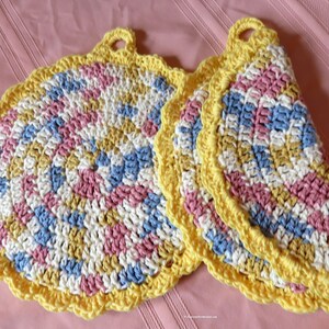 May include: Two crocheted pot holders in a circular shape with a scalloped edge. The pot holders are made with a multi-colored yarn in shades of pink, blue, yellow, and white. Each pot holder has a loop handle.