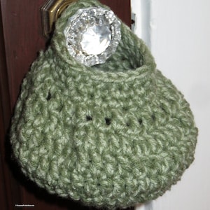 May include: A green crocheted doorstop hanging on a door knob. The doorstop is shaped like a small bag or pouch.