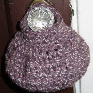May include: A purple and white crocheted doorstop shaped like a pouch, hanging on a door knob.