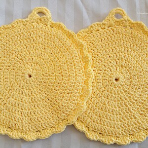 May include: Two yellow crocheted pot holders with a loop handle. The pot holders are round and have a scalloped edge.