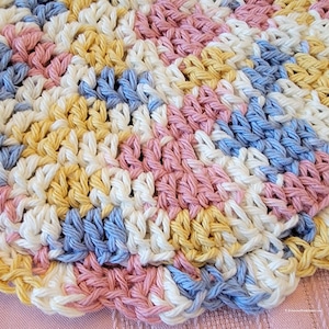 May include: A crocheted round doily with a scalloped edge in shades of pink, yellow, blue, and white.