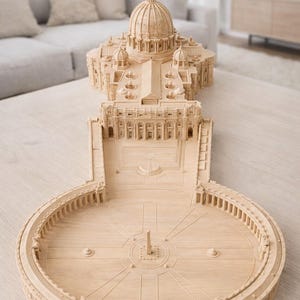 Könnte beinhalten: Ein detailliertes Holzmodell des Petersdoms und des umliegenden Platzes. Das Modell weist komplizierte architektonische Details auf, darunter die Kuppel, die Kolonnaden und der Obelisk in der Mitte des Platzes. Das Modell ist aus hellem Holz gefertigt.