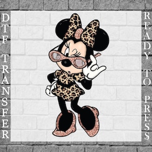 Pode incluir: Transferência DTF Ready to Press com uma personagem de desenho animado Minnie Mouse num vestido, laço e sapatos com estampado de leopardo. Ela usa óculos de sol cor-de-rosa e faz um gesto com a mão. O fundo é uma parede de tijolos brancos.
