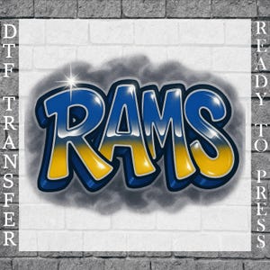May include: A DTF (Direct to Film) transfer design featuring the word "RAMS" in a bold, graffiti-style font. The letters are blue with yellow accents and a silver outline, set against a white brick background. The words "READY TO PRESS" are on the right side.