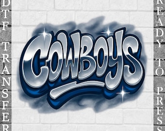 May include: A DTF (Direct to Film) transfer design featuring the word "COWBOYS" in a chrome-like, 3D effect with blue accents. The design is set against a white brick wall background, with "READY TO PRESS" text on the right and "DTF TRANSFER" on the left.