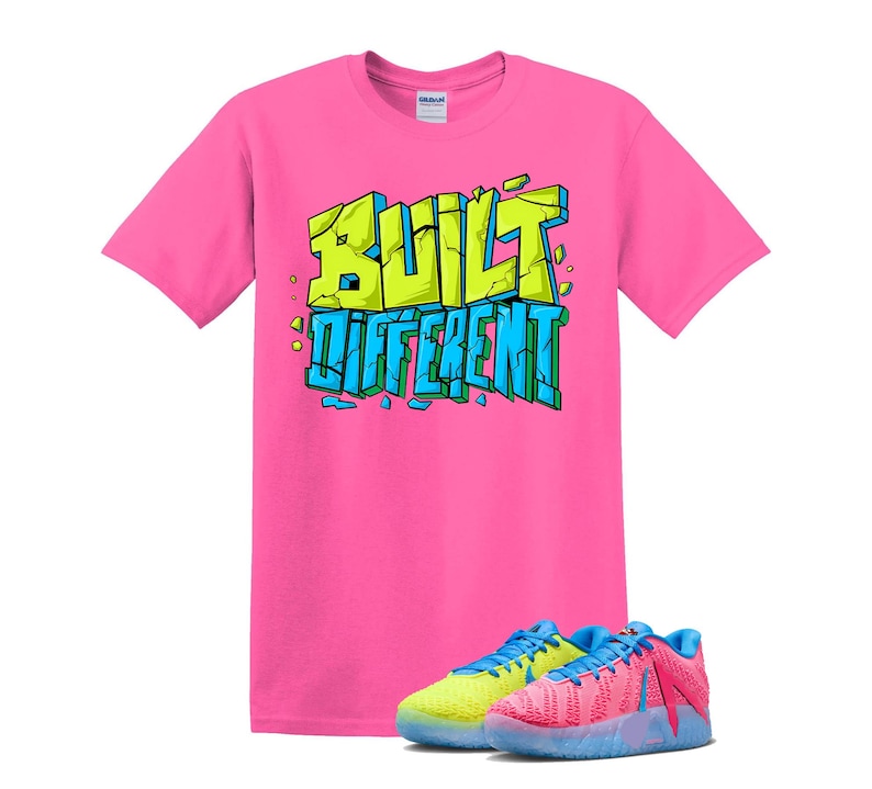 May include: A bright pink t-shirt with the words "BUILT DIFFERENT" in a graffiti-style design. Below the shirt are two pairs of sneakers, one pair is yellow and blue, and the other is pink and blue.