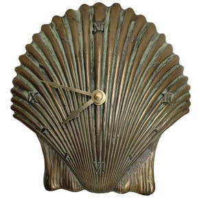 May include: A bronze-colored seashell-shaped clock with Roman numeral hour markers. The clock hands are gold-toned, and the clock face has a textured, ridged design. The clock is a decorative item.