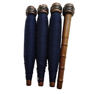 May include: Four antique wooden spools. Three spools are wrapped with dark blue thread, and have metal and wood tops. The fourth spool is made of wood and has a long, cylindrical shape.