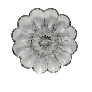 May include: Clear glass serving dish with a scalloped edge and a central starburst design. The dish has a flower-like shape with rounded petal-like sections. The glass is transparent, allowing light to pass through.