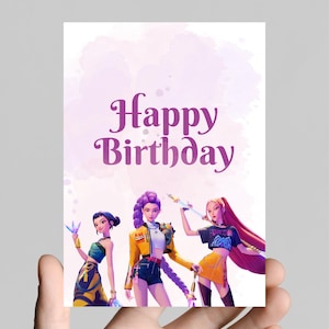 Op de afbeelding: Een wenskaart met de woorden "Happy Birthday" in paars schrift. De kaart toont een illustratie van drie gestileerde vrouwelijke figuren in kleurrijke outfits, die fantasiewapens vasthouden, tegen een aquarel achtergrond.