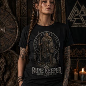 Może przedstawiać: Czarny t-shirt z nadrukiem graficznym przedstawiającym wojownika trzymającego włócznię i tarczę, otoczonego kolistą runiczną obwódką. Pod ilustracją znajduje się napis RUNE KEEPER oraz KEEPER OF THE OLD CODE wykonany przetartą czcionką.