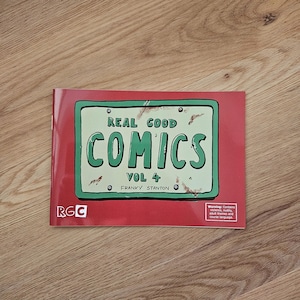 May include: A comic book titled "Real Good Comics Vol 4" with a red cover. The cover features a green license plate design with the title in large, bold letters. The author's name is Franky Stanton. A warning is printed on the bottom right.