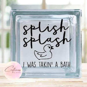 May include: A clear glass block with a black vinyl decal that reads "Splish Splash I Was Takin' A Bath". A cartoon rubber duck is also included in the design.