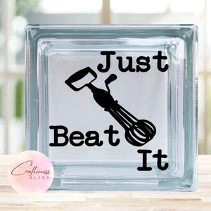 May include: A glass block with a black silhouette of a hand mixer and the text "Just Beat It".