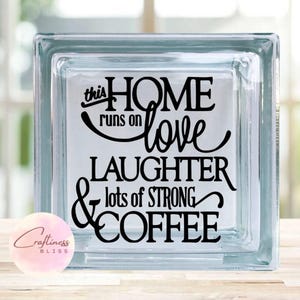 May include: A glass block with a black vinyl decal that reads "This home runs on love, laughter, & lots of strong coffee".