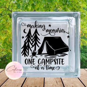 May include: A glass block with a black and white design of a campfire, trees, and a tent. The text "Making memories one campsite at a time" is written on the block.