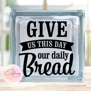 May include: A clear glass block with a black vinyl decal that reads "Give us this day our daily bread".