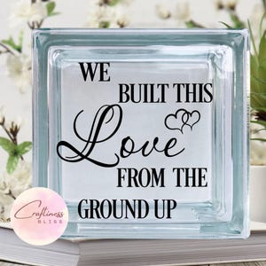 May include: A clear glass block with the text "We built this love from the ground up" and two hearts.