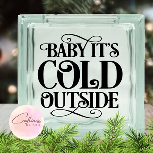 May include: A clear glass block with a black vinyl decal that reads "Baby It's Cold Outside".