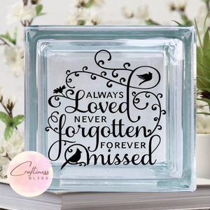 May include: A glass block with a black vinyl decal that reads "Always Loved Never Forgotten Forever Missed". The decal features a floral design with birds.