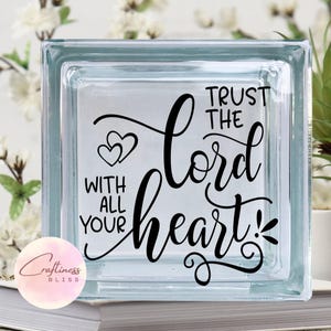 May include: A glass block with the words "Trust the Lord with all your heart" in black cursive lettering. Two small hearts are above the word "Lord".