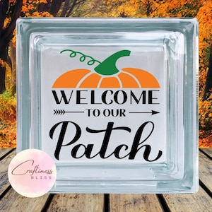 May include: A glass block with a pumpkin and the text "Welcome to our Patch" in black lettering. The pumpkin is orange with a green stem and leaves.