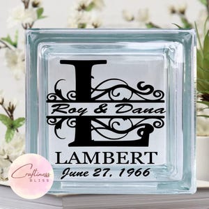 May include: A glass block with a black and white design featuring a large letter L, a decorative scroll, and the text "Roy & Dana Lambert June 27, 1966".