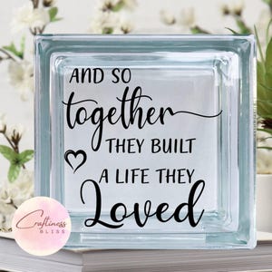 May include: A glass block with the text "And so together they built a life they loved" in black lettering. The text is in a cursive font and includes a small heart symbol.