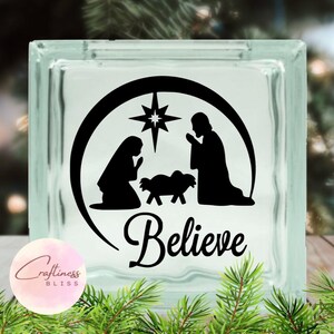 May include: A glass block with a black and white silhouette of the nativity scene with a star above the manger. The text "Believe" is written below the scene.